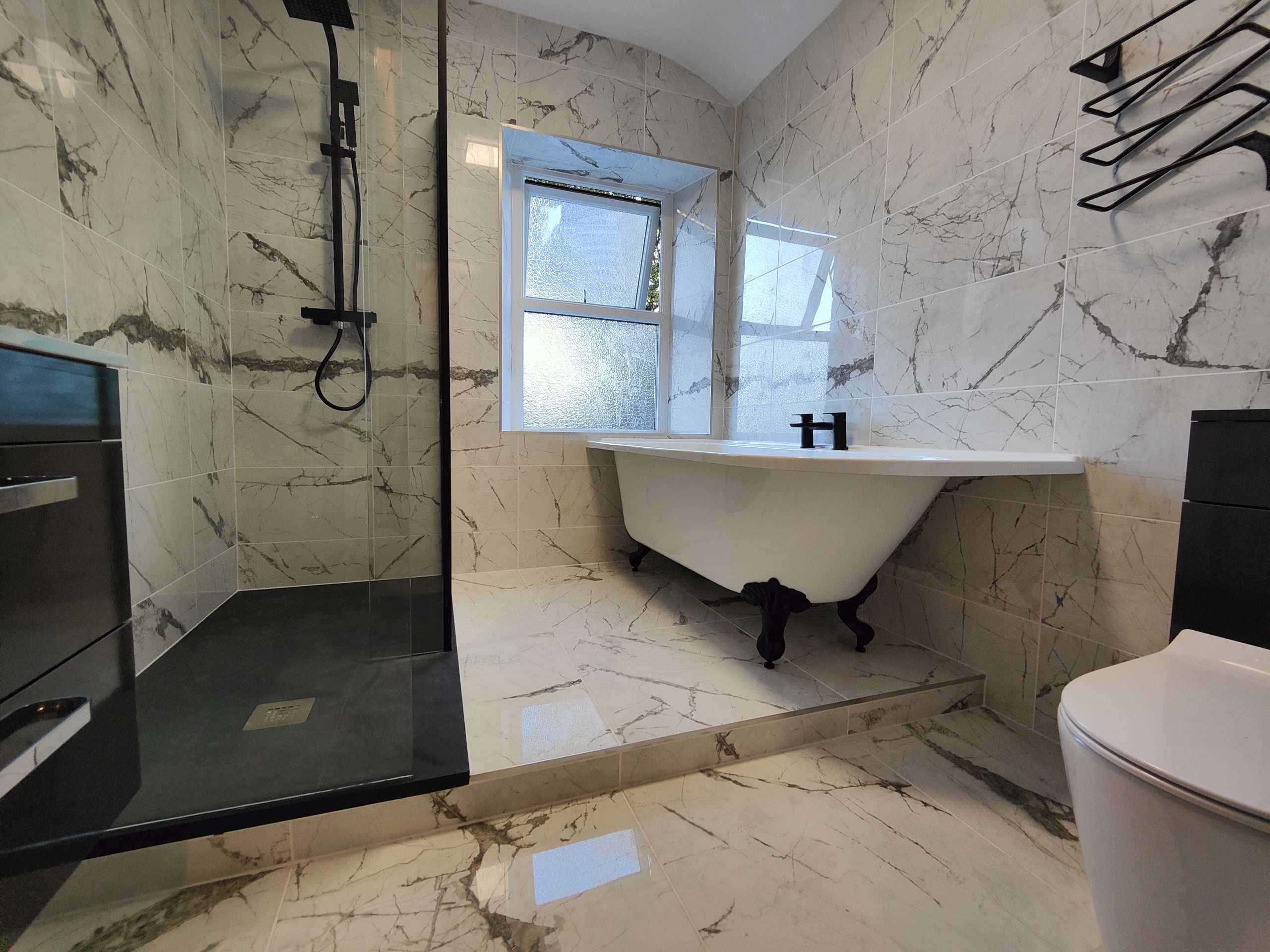 Marble-tiled bathroom with freestanding bath and black-framed shower
