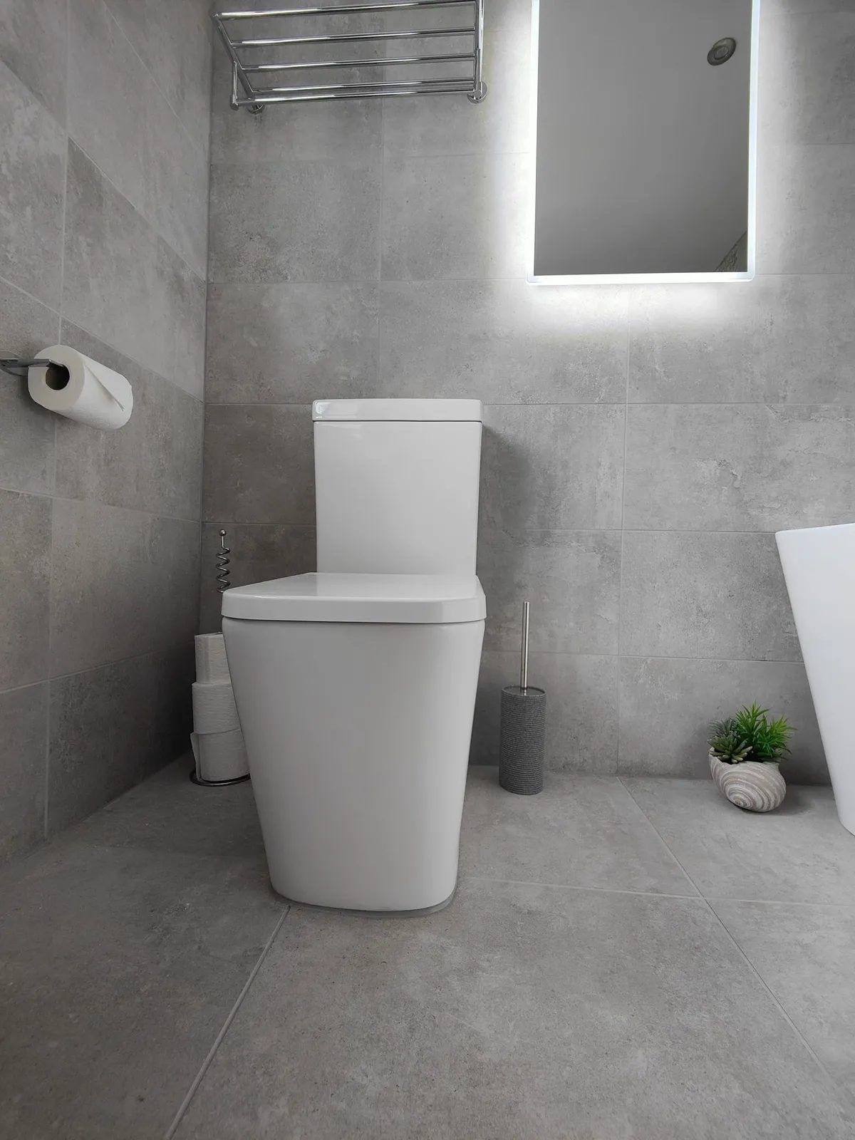 Grey tiled bathroom with modern toilet and LED-lit mirror